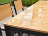 Park City Dining Table in the rain black frame natural teak on brick patio